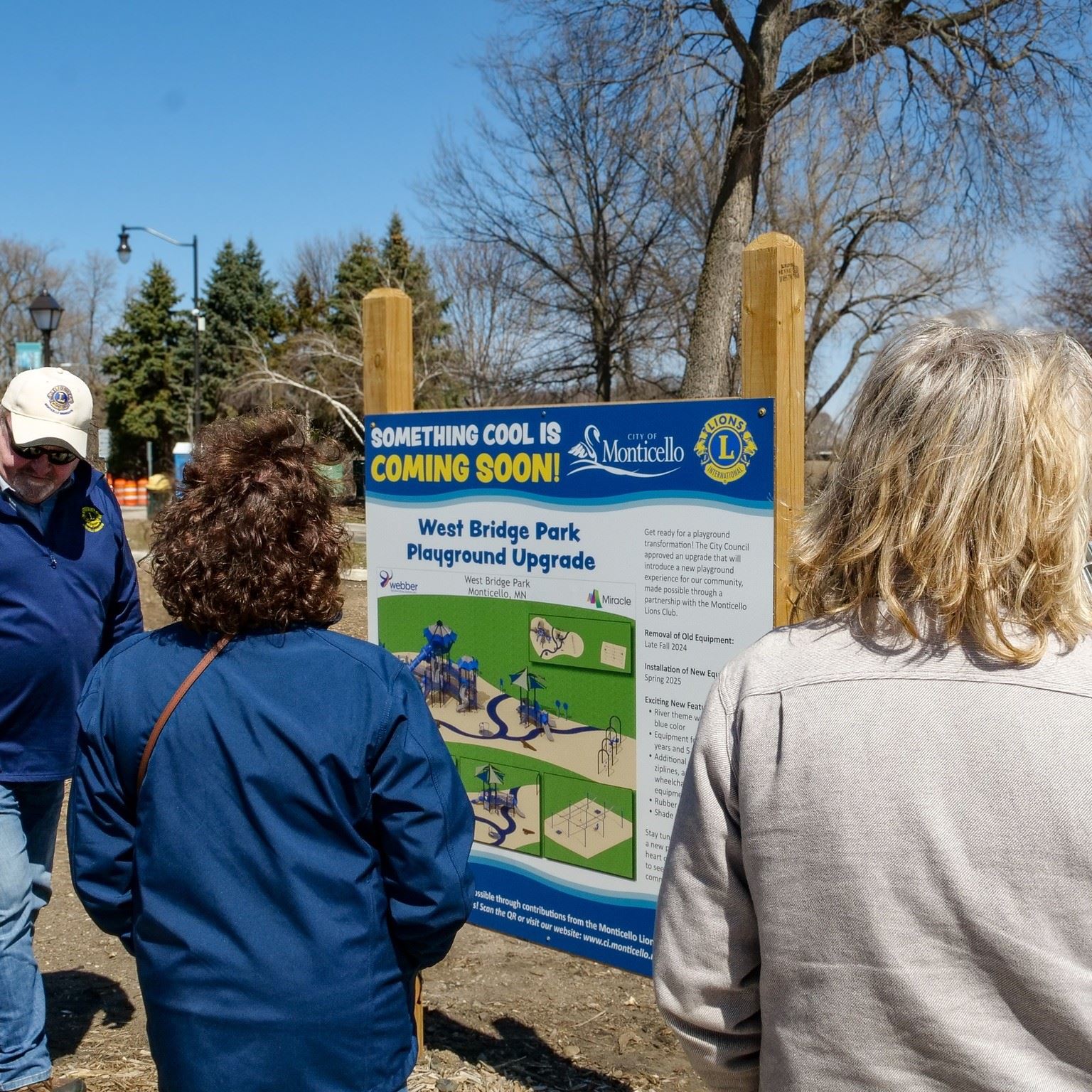 Two women and a man looking at a park sign.