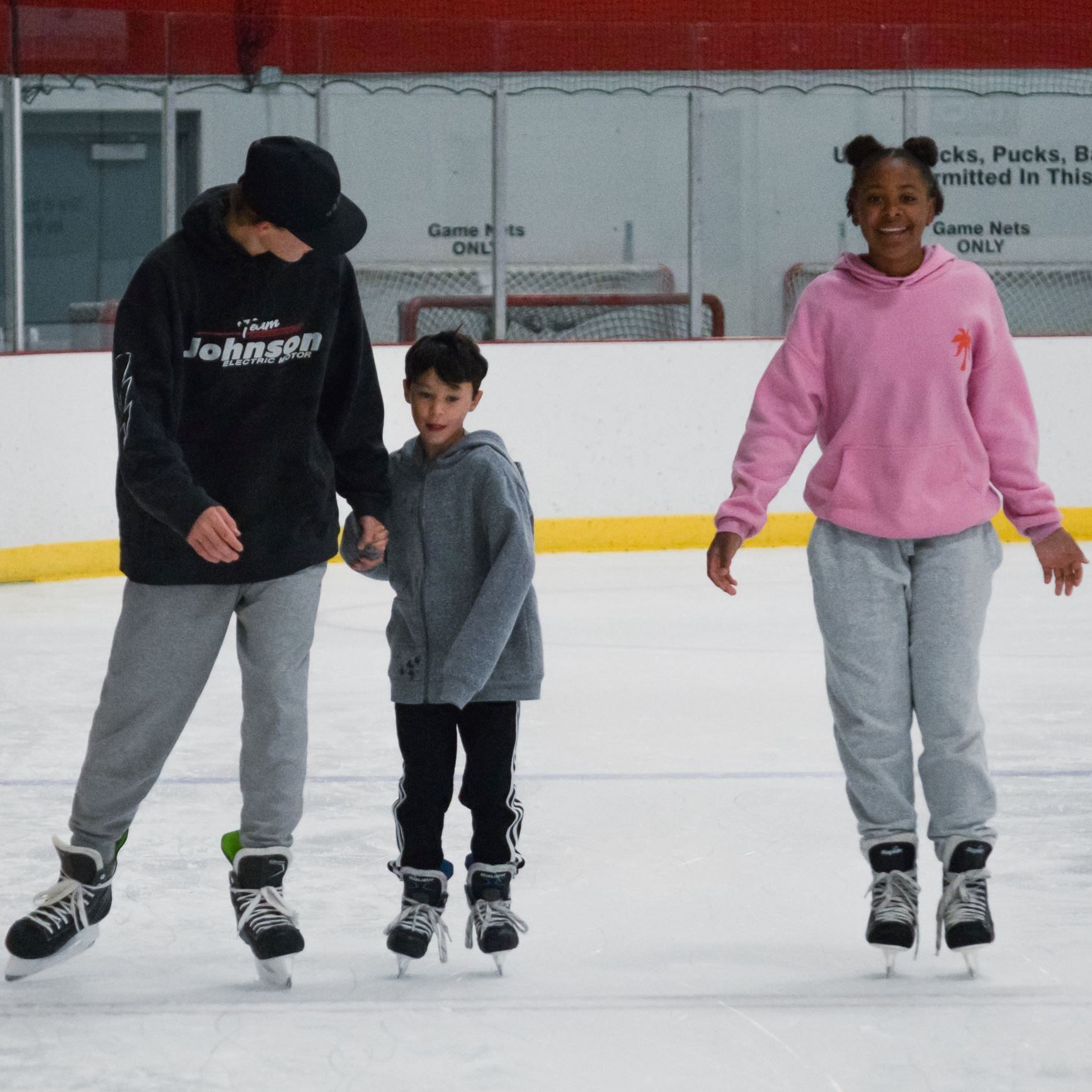 Two young adults and a child skating in the ice arena.